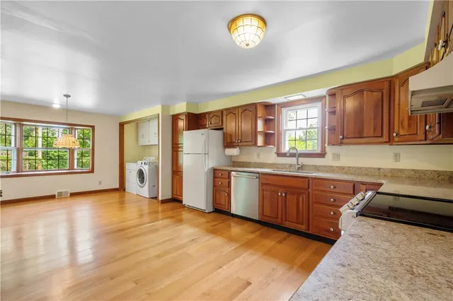 a kitchen with stainless steel appliances granite countertop a sink dishwasher stove and a refrigerator with wooden floor