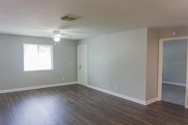 an empty room with wooden floor chandelier fan and windows