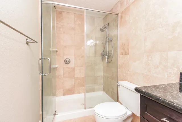 a bathroom with a granite countertop bathtub shower sink vanity and toilet