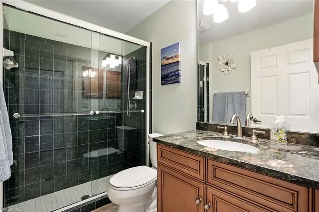 a bathroom with a granite countertop sink a toilet a mirror and shower