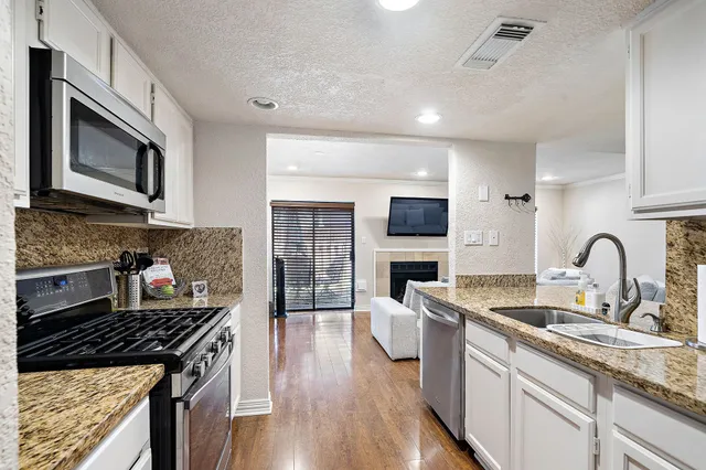 a kitchen with stainless steel appliances granite countertop a stove top oven a sink dishwasher and cabinets with wooden floor