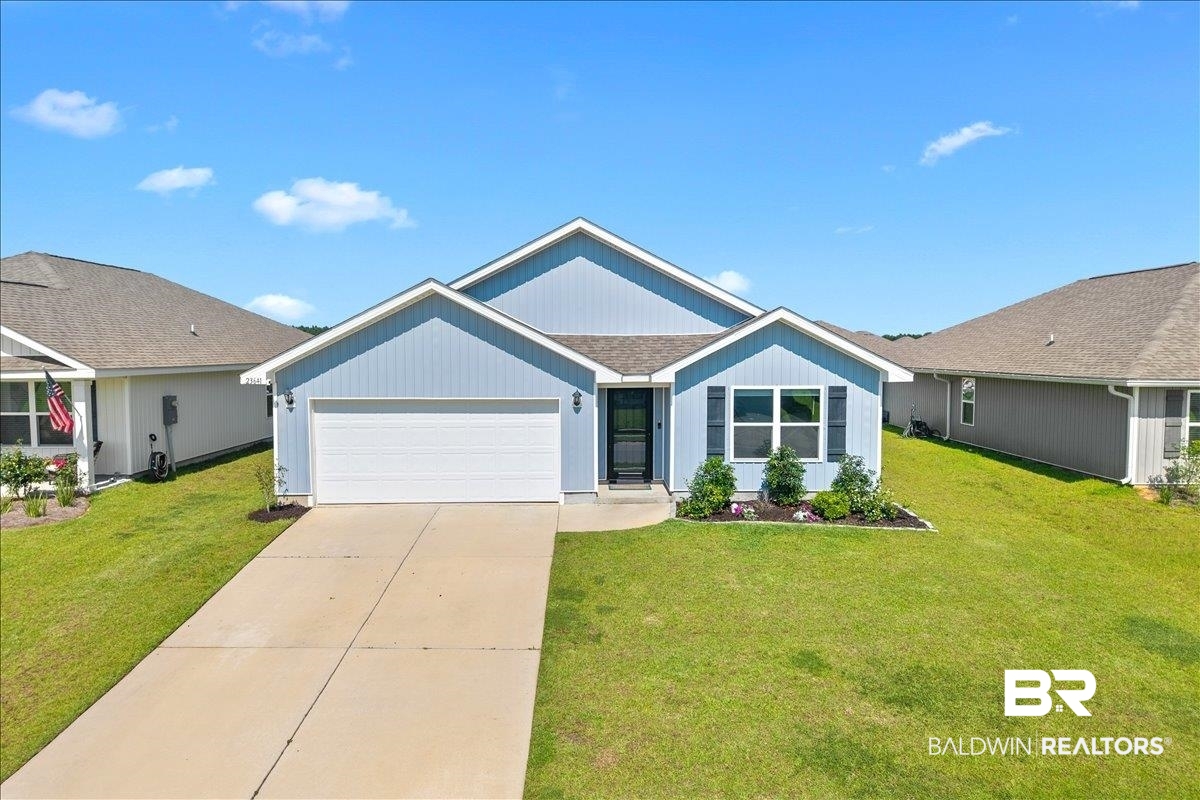 23641 Unbridled Loop Daphne, AL 36526 - Photo 2 of 40 Light blue siding exterior featuring a prominent gable roofline, attached two-car garage, concrete driveway, front entry with black door, and front landscaping with shrubs