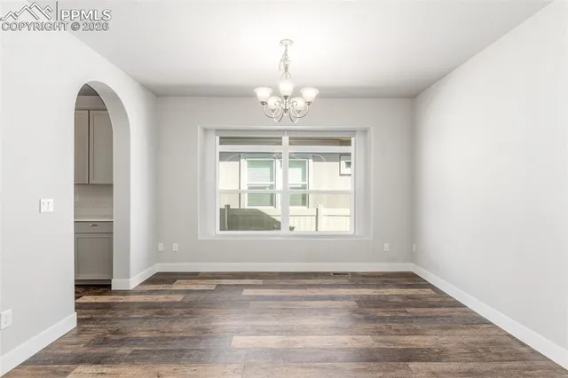 an empty room with wooden floor chandelier and windows