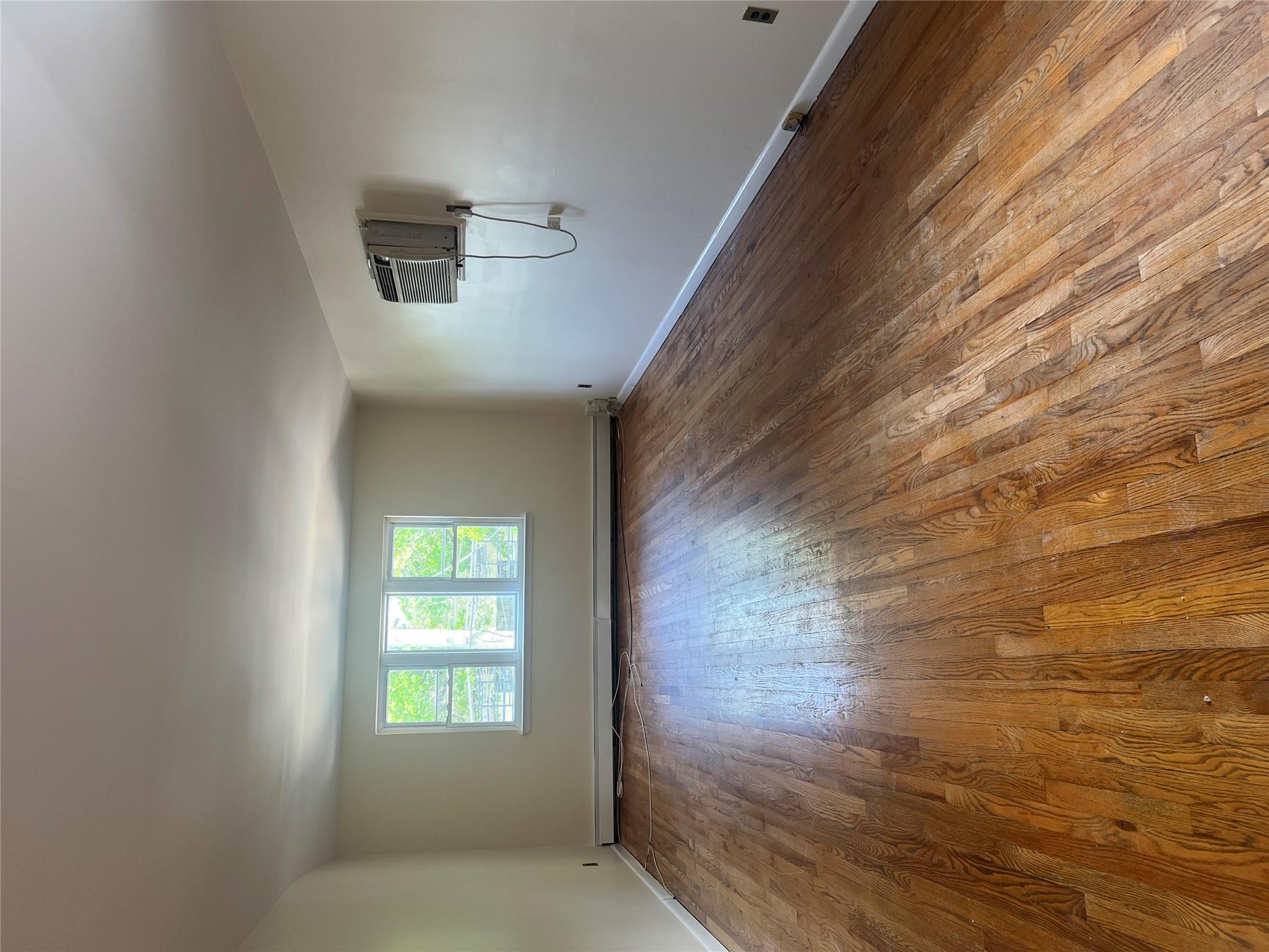 206-18 45th Road, Unit SECOND Queens, NY 11361 - Photo 6 of 14 Unfurnished room with dark wood-type flooring, an AC wall unit, and baseboards