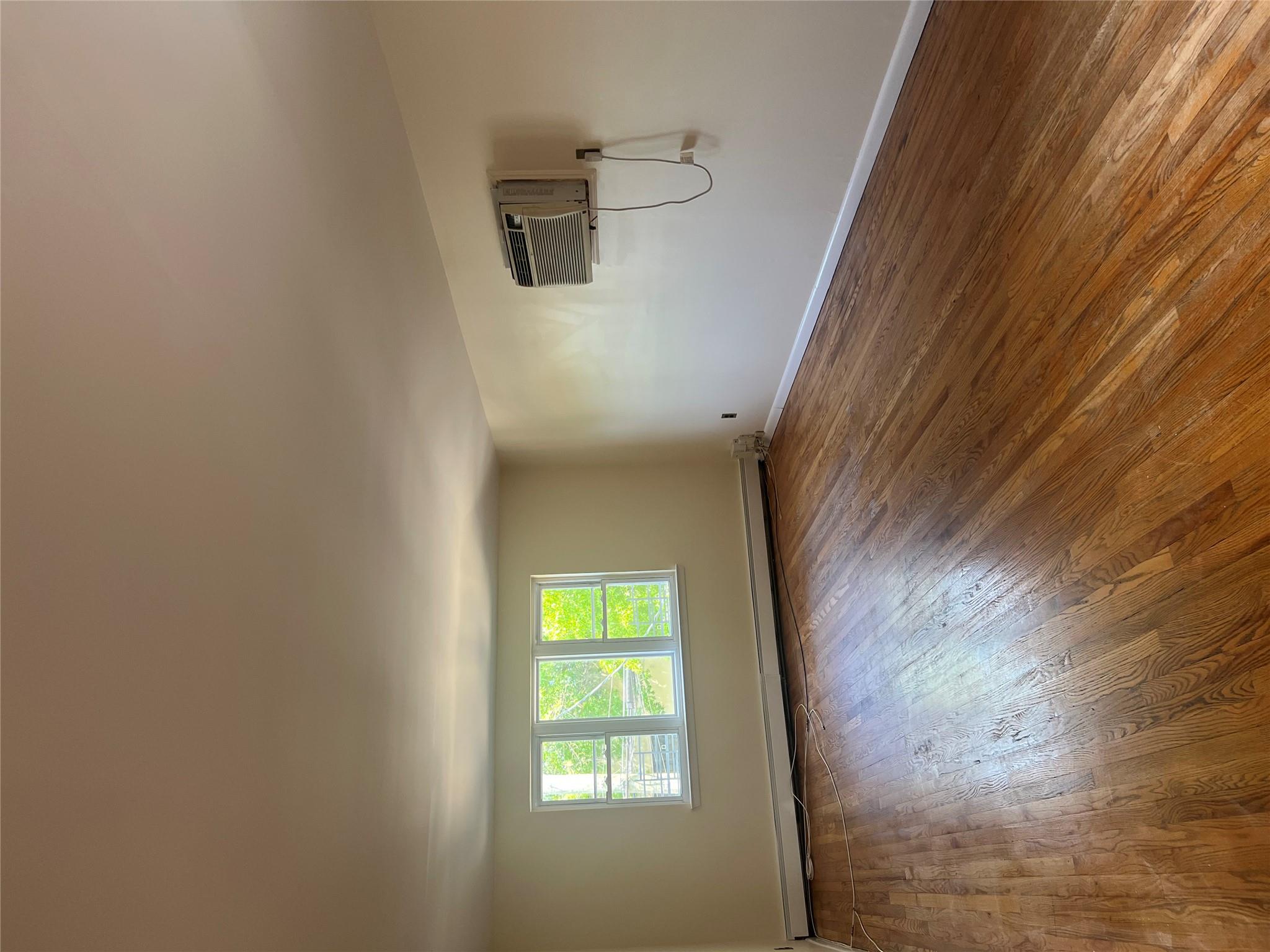 206-18 45th Road, Unit SECOND Queens, NY 11361 - Photo 7 of 14 Empty room with baseboard heating, a wall mounted AC, hardwood / wood-style floors, and baseboards