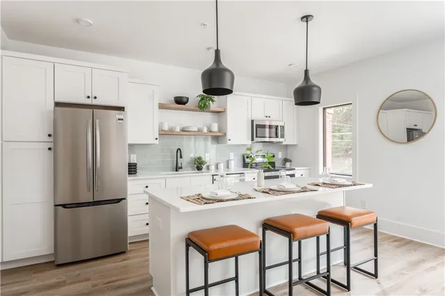 a kitchen with stainless steel appliances granite countertop white cabinets a refrigerator a sink a stove and chairs with wooden floor