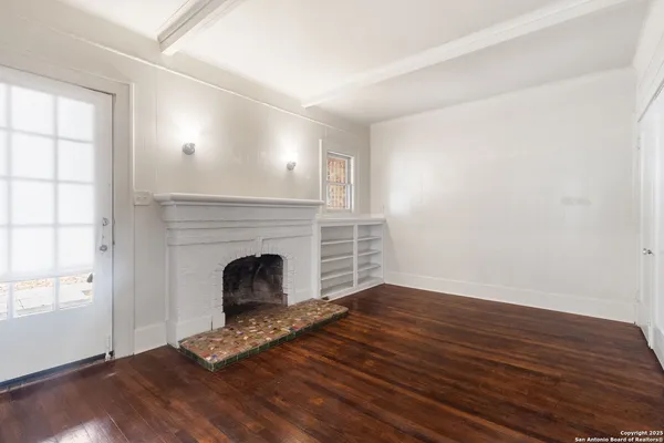a view of an empty room with wooden floor fireplace and a window