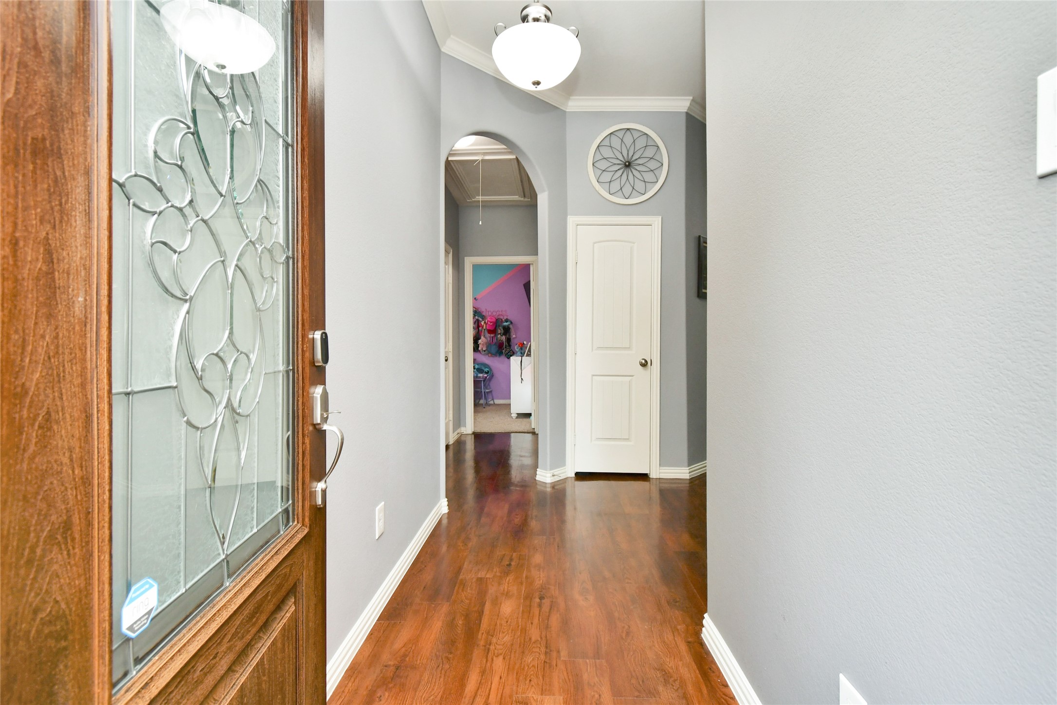652 Maple Point Drive East Conroe, TX 77301 - Photo 5 of 35 This photo showcases a welcoming entryway with a decorative glass front door, elegant hardwood floors, and a modern light fixture. The hallway leads to an arched doorway, adding charm and character to the space.