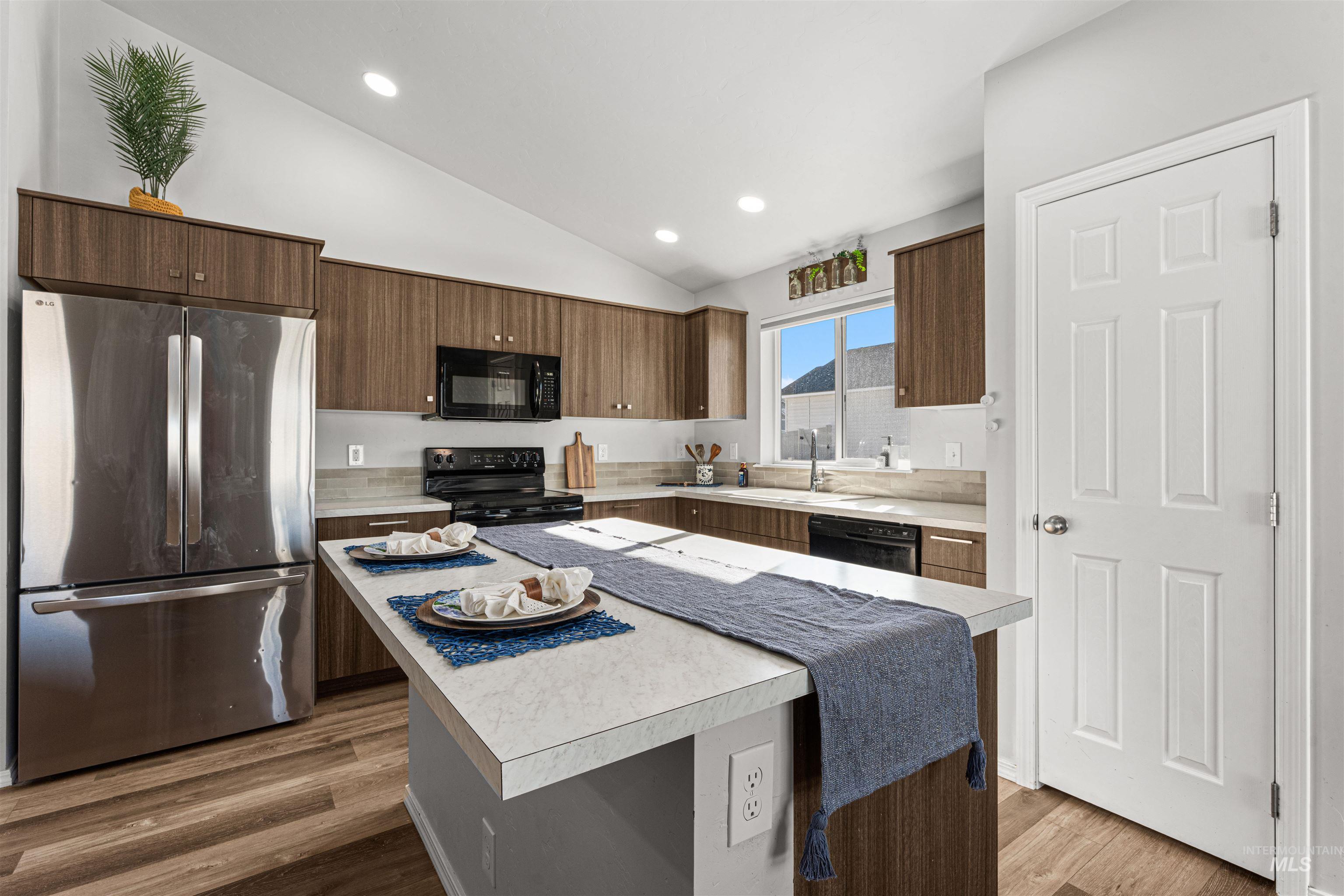12342 Noreen Street Caldwell, ID 83607 - Photo 17 of 42 Kitchen with black appliances, light countertops, lofted ceiling, dark wood finish cabinets, and a center island