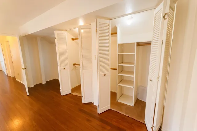 a view of an empty room with wooden floor and a bathroom
