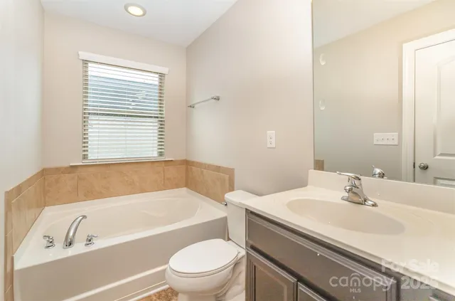 a bathroom with a granite countertop bathtub sink vanity mirror and toilet