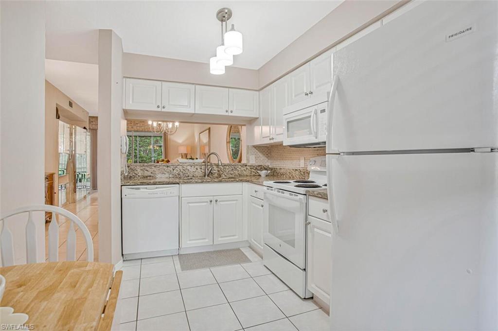 6605 Huntington Lakes Circle, Unit 103 Naples, FL 34119 - Photo 5 of 30 a kitchen with granite countertop a refrigerator a sink and white cabinets