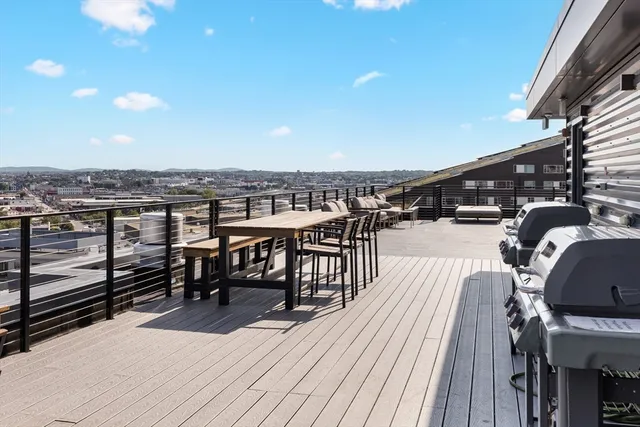 a view of a roof deck with table and chairs a barbeque with wooden floor and city view