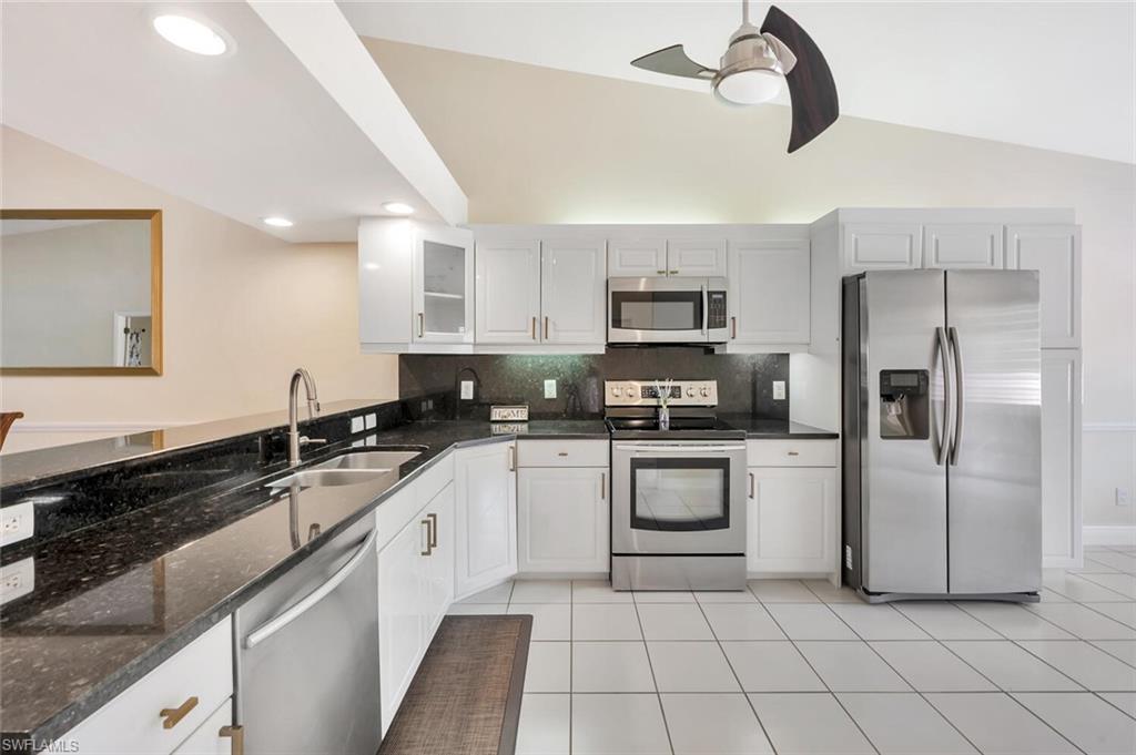 6720 Beach Resort Drive, Unit 10 Naples, FL 34114 - Photo 4 of 34 Kitchen with stainless steel appliances, ceiling fan, decorative backsplash, glass insert cabinets, and dark stone counters