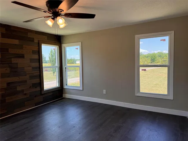 an empty room with wooden floor chandelier fan and windows