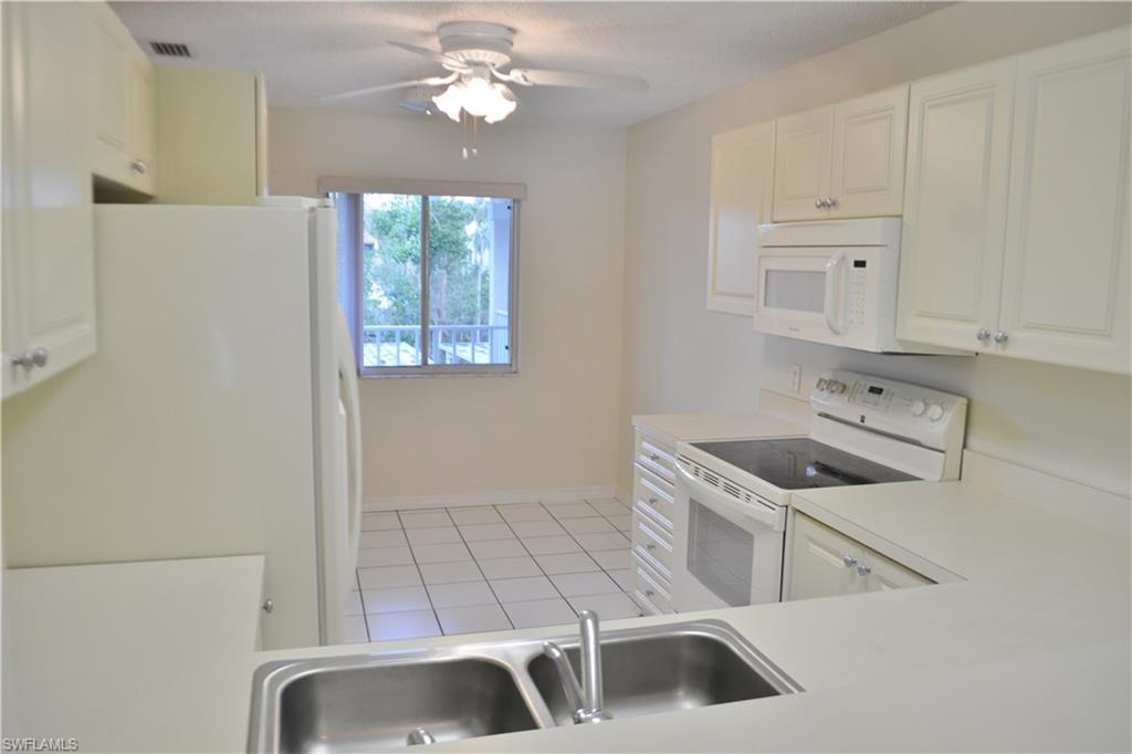 240 Timber Lake Circle, Unit D202 Naples, FL 34104 - Photo 6 of 23 a kitchen with white cabinets a sink a stove and dishwasher