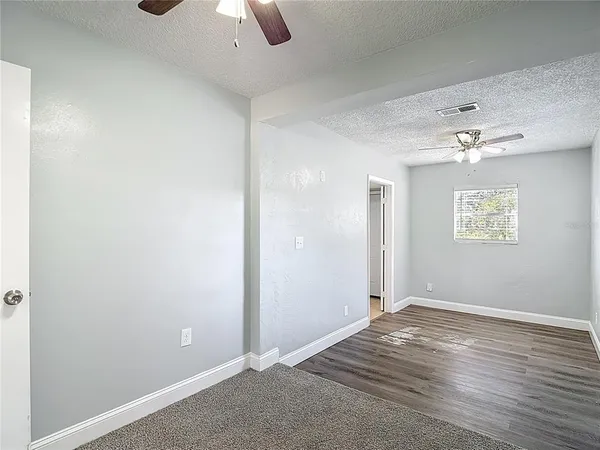 an empty room with a chandelier fan and wooden floor