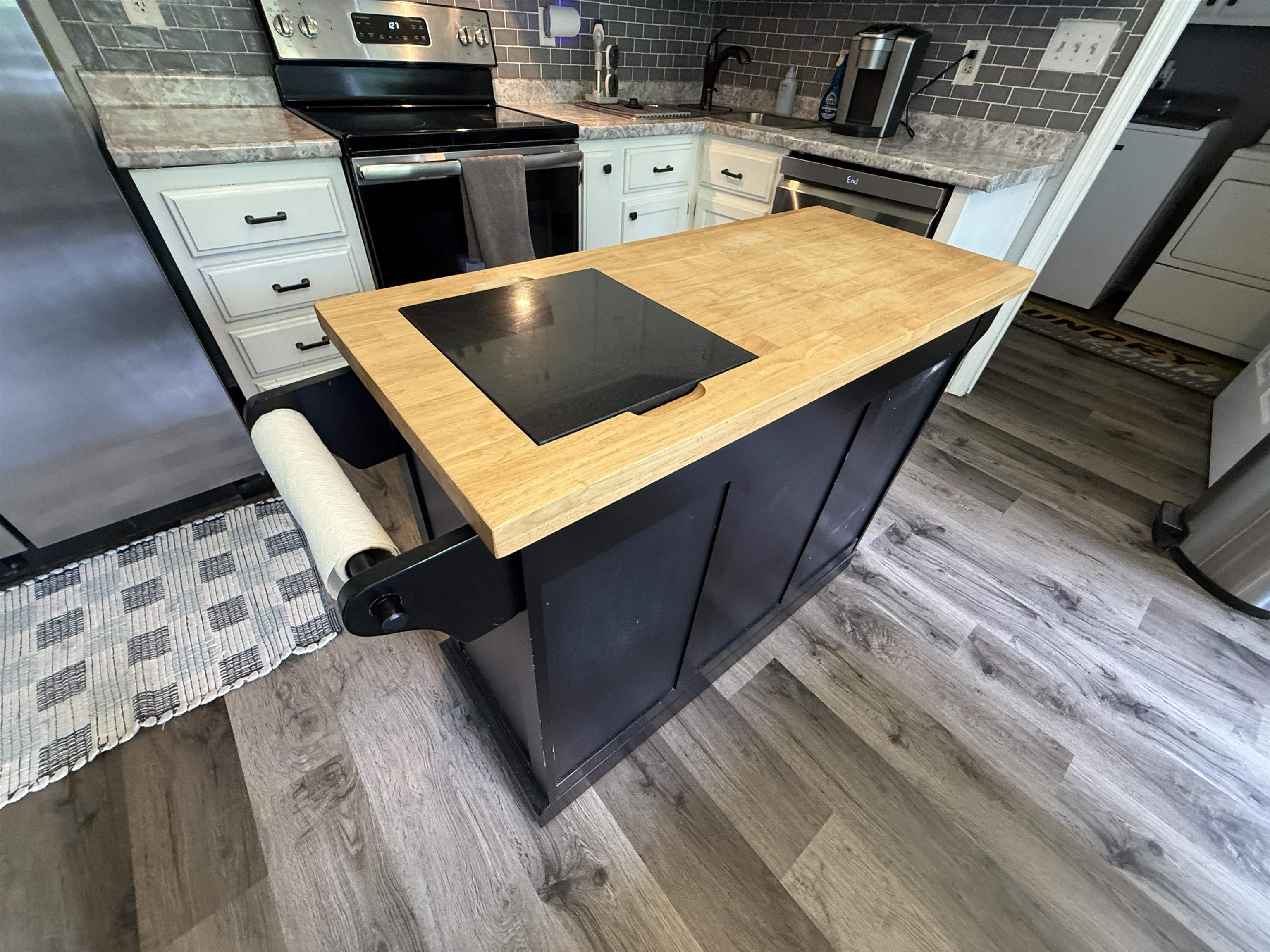 185 Mignon Road Atoka, TN 38004 - Photo 15 of 34 Kitchen featuring a black island with a butcher block countertop and built-in cooktop, light gray wood-finish flooring, white cabinetry with black hardware, stone-look countertops, and a gray subway tile backsplash