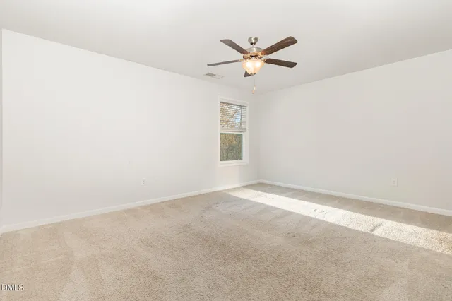 an empty room with a ceiling fan and carpet