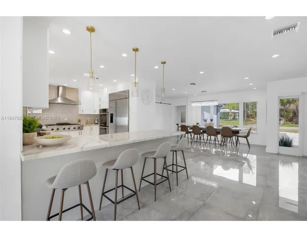 a kitchen with stainless steel appliances kitchen island granite countertop a table chairs and a view of living room