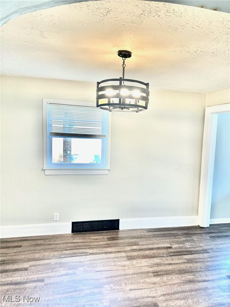 1389 Diagonal Road Akron, OH 44320 - Photo 14 of 20 Unfurnished dining area featuring a chandelier, wood finished floors, baseboards, and a textured ceiling