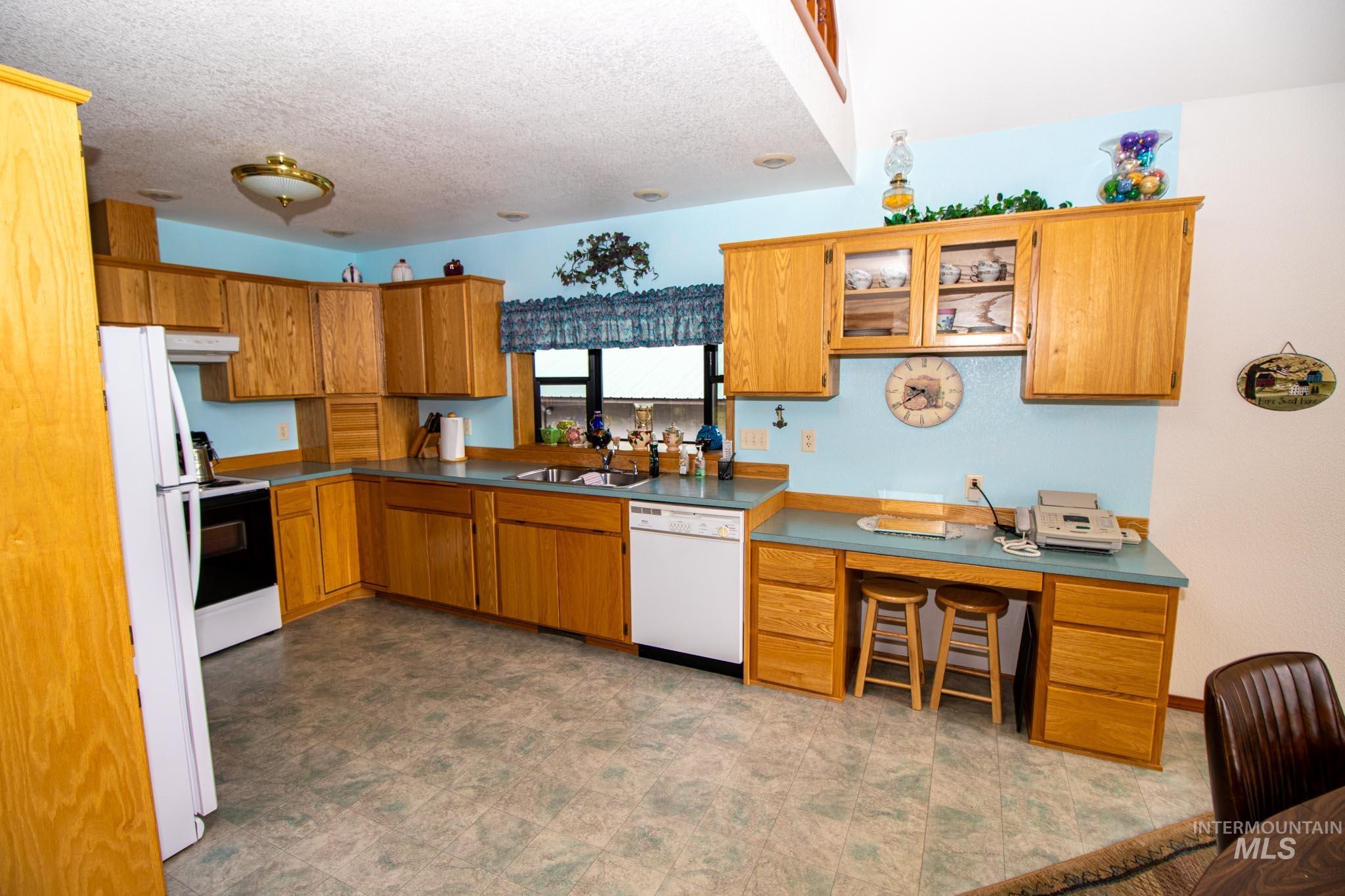 20888 Upper Fords Creek Road Weippe, ID 83553 - Photo 13 of 50 Kitchen featuring white appliances, wood finish cabinetry, a textured ceiling, glass fronted cabinets, and dark countertops
