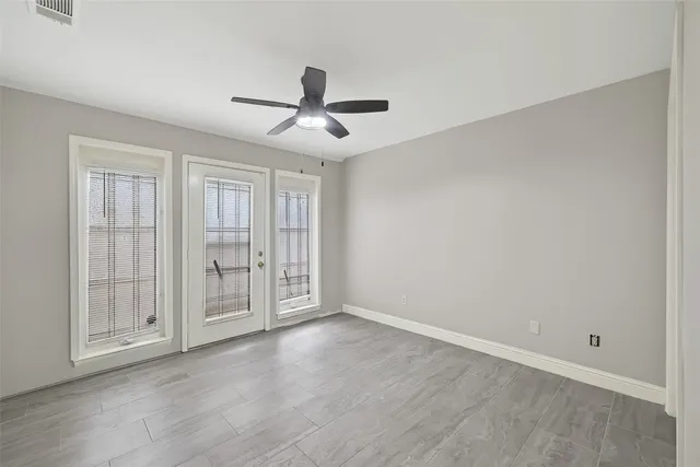 an empty room with wooden floor fan and windows