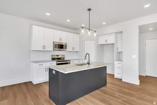547 North Hvn Drive Mapleton, UT 84664 - Photo 7 of 23 Two tone kitchen featuring light wood-type flooring, stainless steel appliances, light stone countertops, a kitchen island with sink, and decorative light fixtures