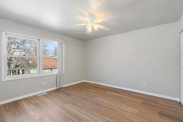 an empty room with wooden floor chandelier fan and windows