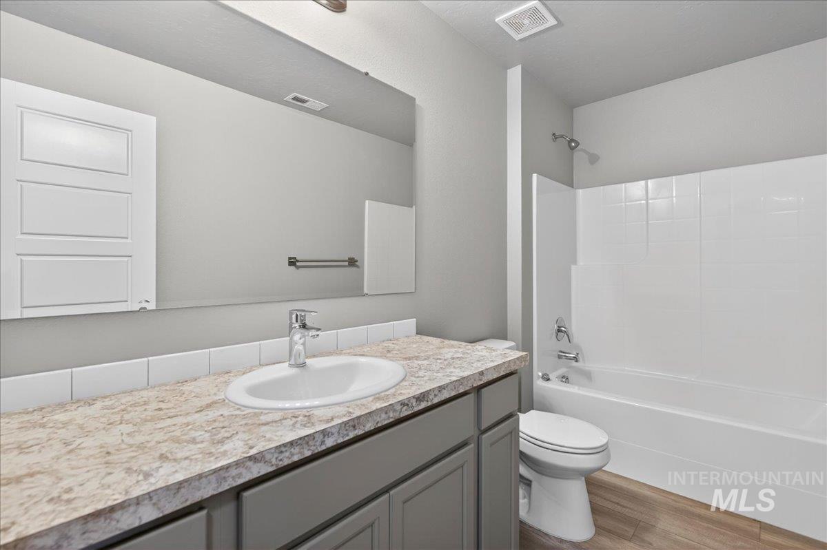 2505 East Goldstone Street Meridian, ID 83642 - Photo 20 of 28 Bathroom featuring a wood-finish floor, a bathtub with a white subway tile surround, a vanity with gray cabinetry, a speckled countertop, and a built-in mirror