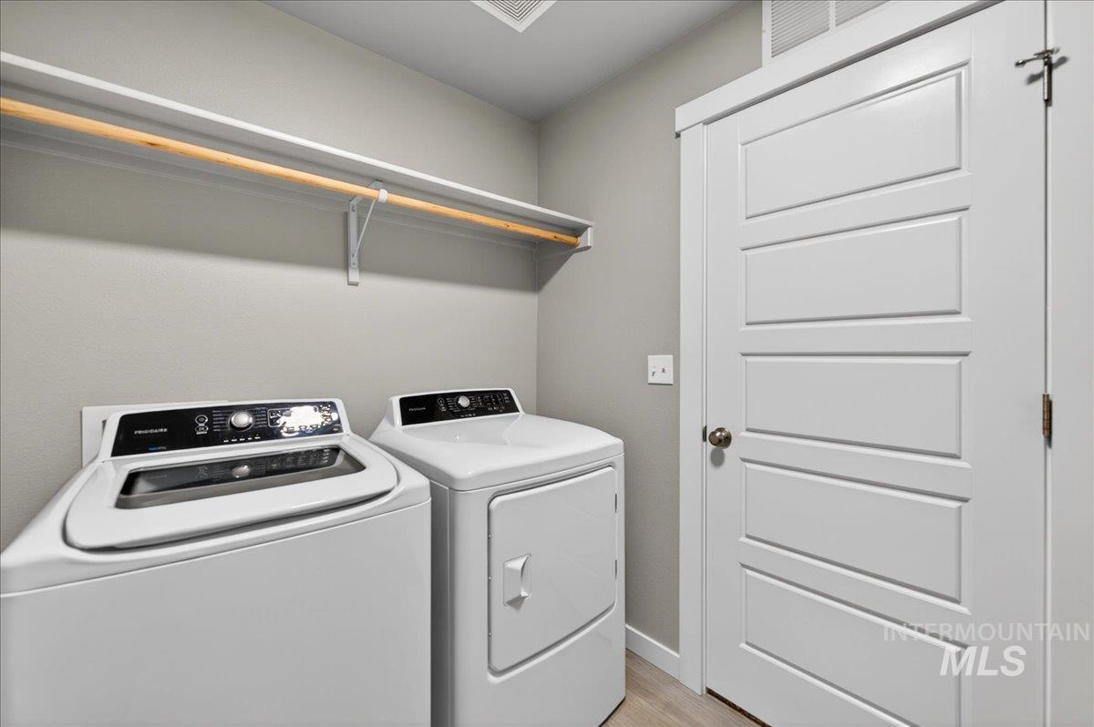 2505 East Goldstone Street Meridian, ID 83642 - Photo 21 of 28 Dedicated laundry area featuring a top-load washer and front-load dryer, overhead shelving with hanging rod, and light wood-finish flooring