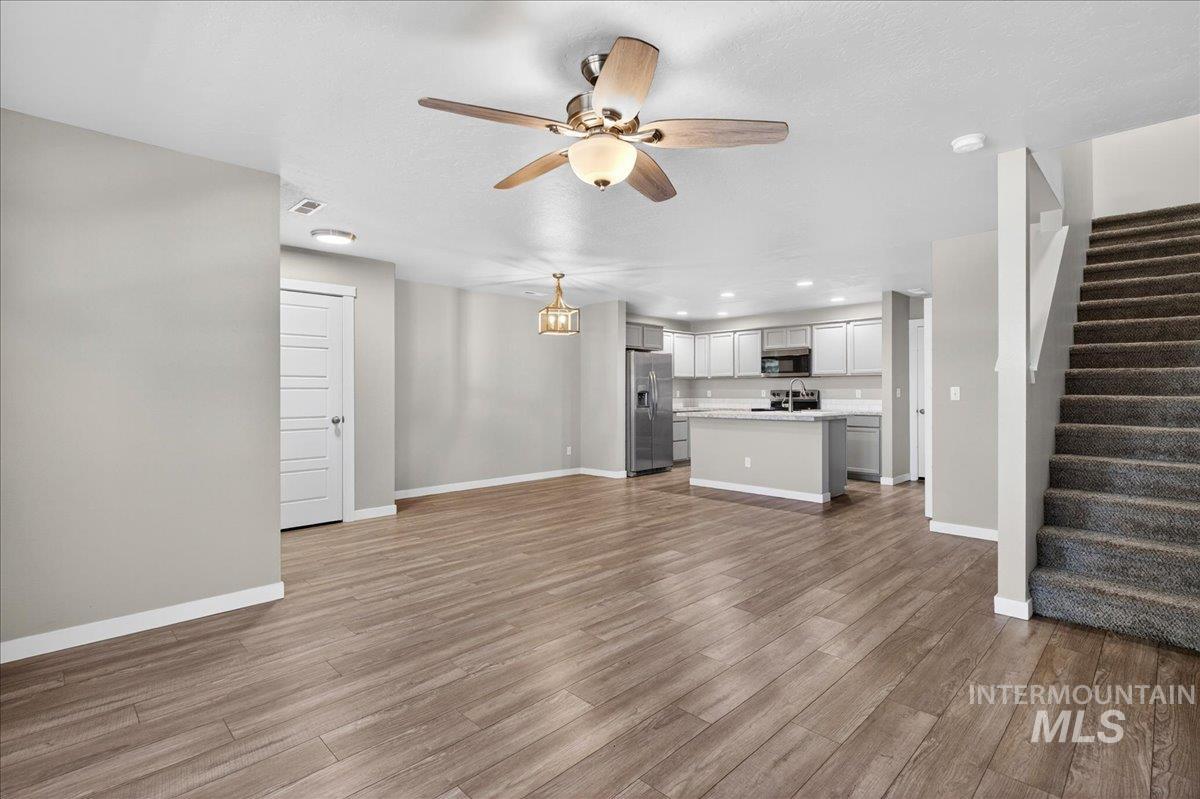 2505 East Goldstone Street Meridian, ID 83642 - Photo 3 of 28 Open-concept living space featuring wood-finish flooring, a contemporary kitchen with light-colored cabinetry and stainless steel appliances, a ceiling fan with integrated lighting, and a carpeted staircase