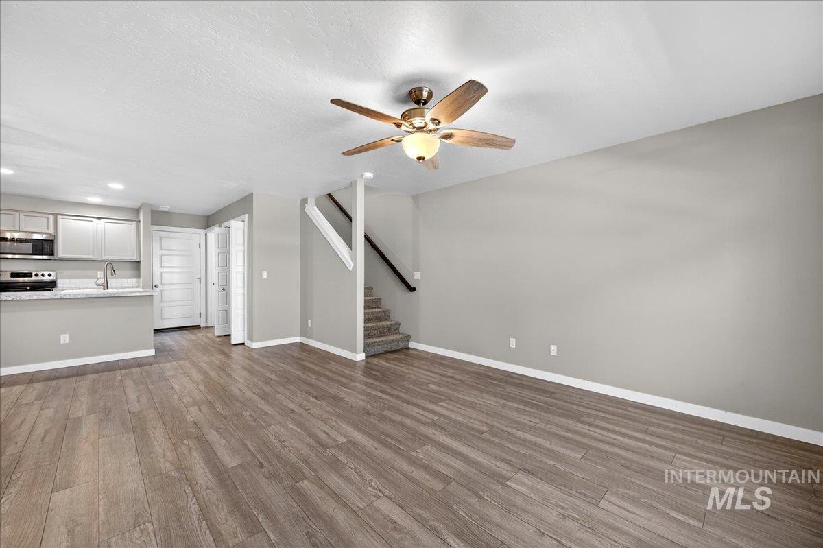 2505 East Goldstone Street Meridian, ID 83642 - Photo 4 of 28 Open-concept living space featuring wood-finish flooring, a ceiling fan with integrated lighting, and a modern kitchen with light gray cabinetry, stainless steel appliances, and a breakfast bar