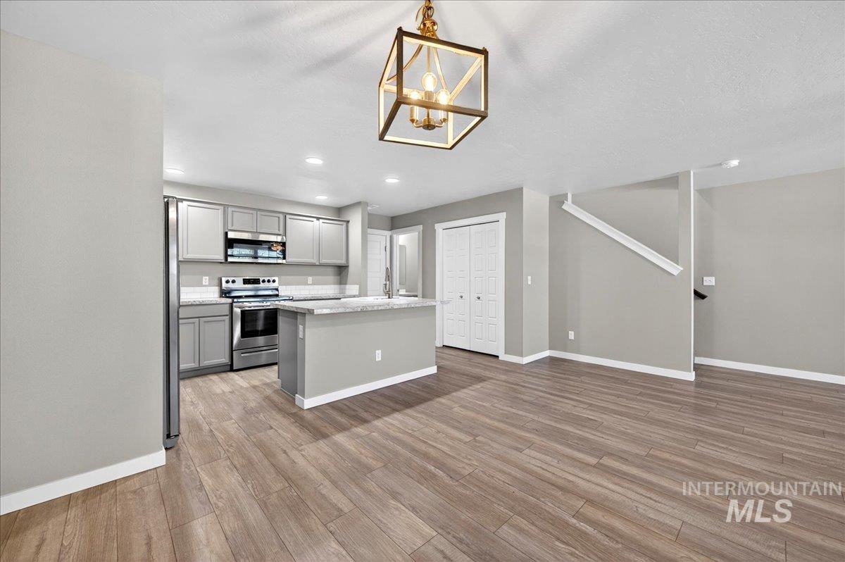 2505 East Goldstone Street Meridian, ID 83642 - Photo 5 of 28 Open-concept living area featuring wood-finish flooring, a contemporary kitchen with stainless steel appliances, light gray cabinetry, and a central island with a stone-look countertop