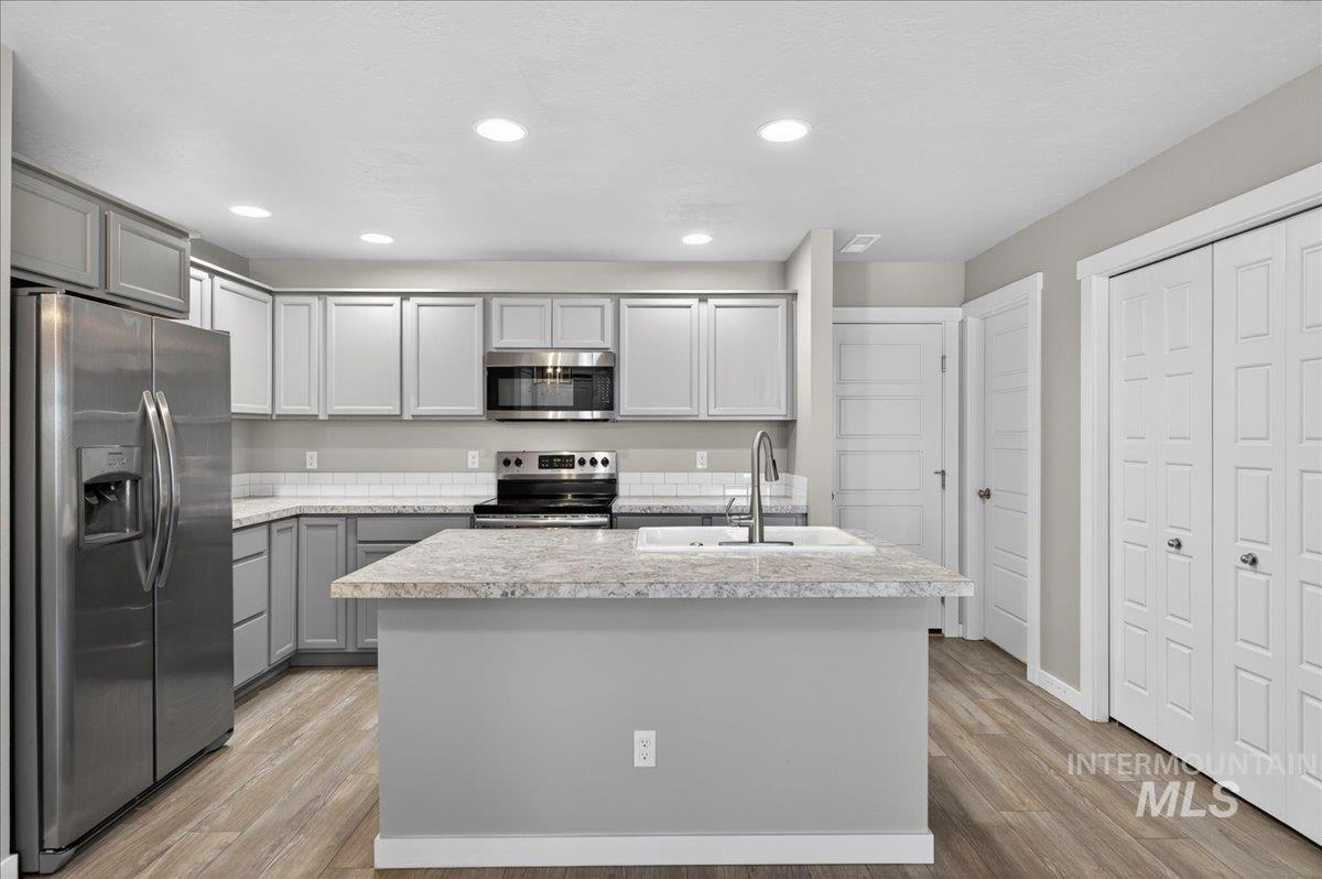 2505 East Goldstone Street Meridian, ID 83642 - Photo 7 of 28 Open-concept kitchen featuring gray shaker-style cabinetry, stainless steel appliances, an island with a built-in sink, wood-finish flooring, and recessed lighting