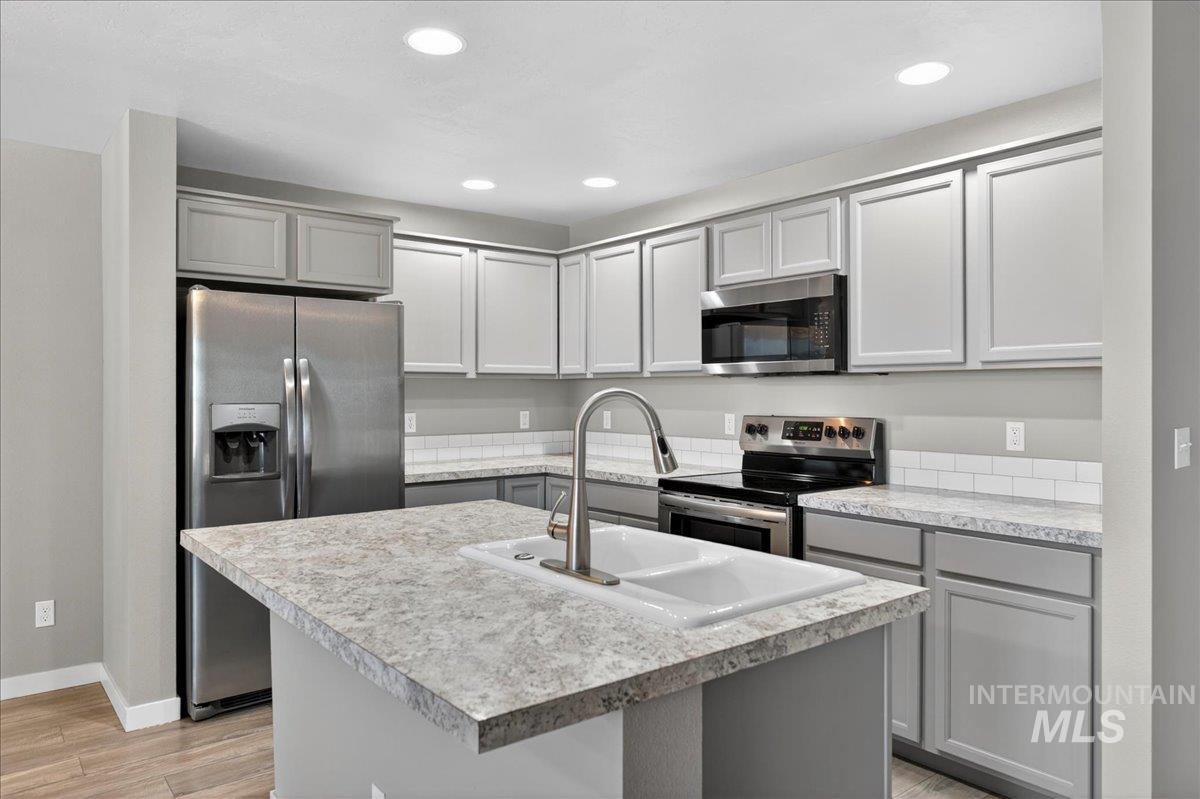 2505 East Goldstone Street Meridian, ID 83642 - Photo 8 of 28 Kitchen featuring a central island with a double basin sink, stainless steel appliances, light gray cabinetry, and a subway tile backsplash