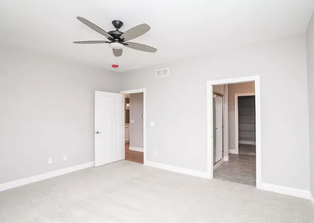 an empty room with ceiling fan and windows