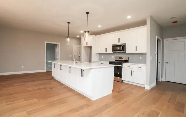 a large white kitchen with kitchen island granite countertop a stove top oven a sink and white cabinets
