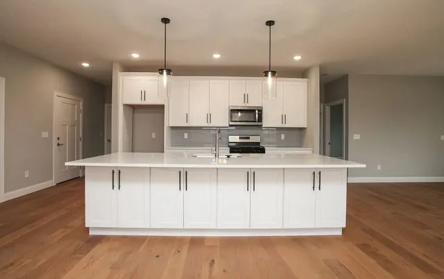 a kitchen with stainless steel appliances kitchen island granite countertop a sink a microwave a refrigerator and white cabinets