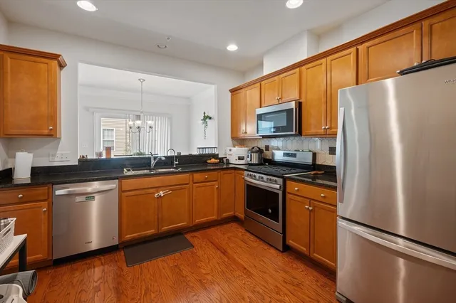 a kitchen with stainless steel appliances granite countertop a refrigerator a sink dishwasher a stove with wooden cabinets and floor