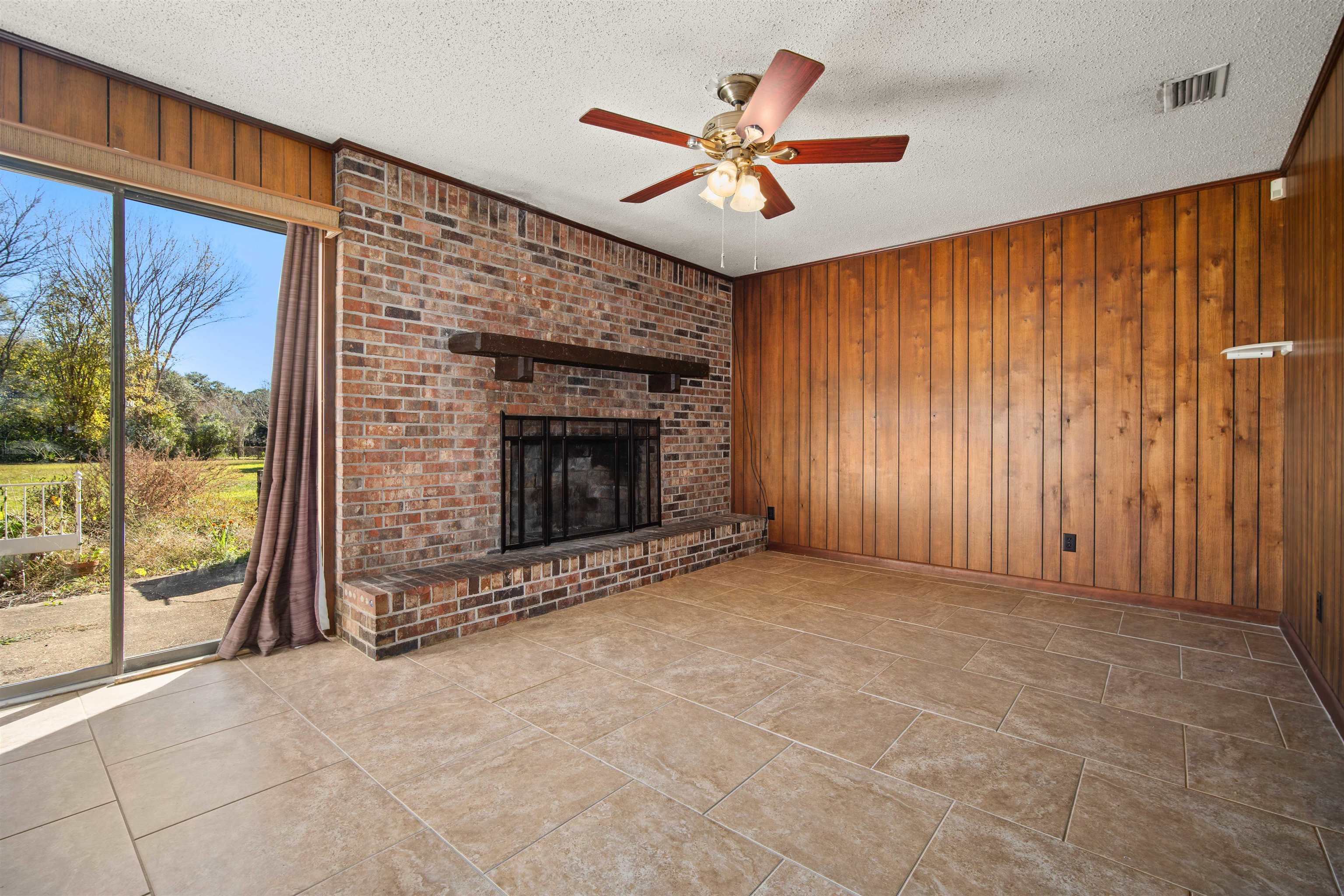 10285 Argyle Road Irvington, AL 36544 - Photo 6 of 28 Unfurnished living room featuring wood walls, a textured ceiling, a fireplace, ceiling fan, and light tile patterned floors
