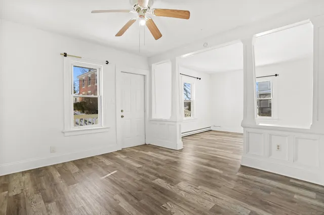 an empty room with wooden floor chandelier fan and windows