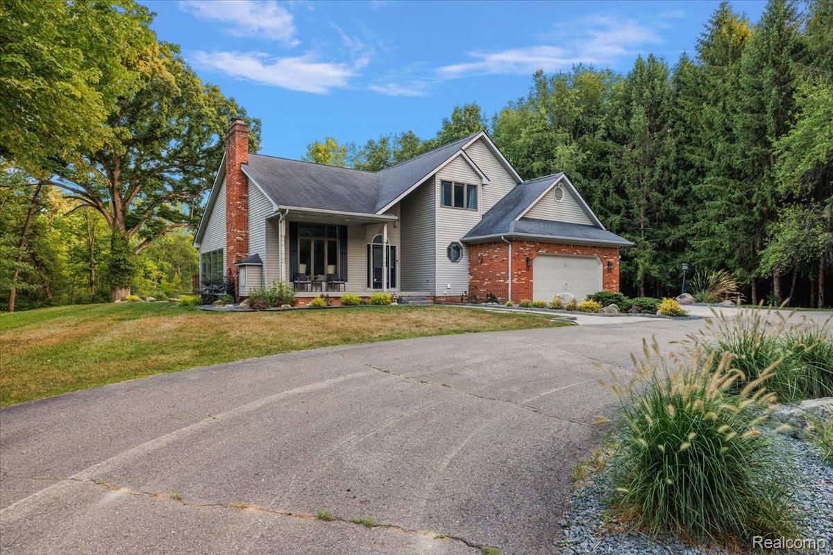 707 West Sutton Road Metamora, MI 48455 - Photo 5 of 84 Exterior featuring brick and siding finishes, an attached garage, a covered front porch, a prominent brick chimney, and a paved driveway