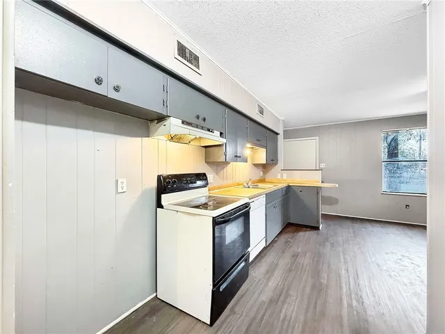 a kitchen with a stove a sink and white cabinets with wooden floor