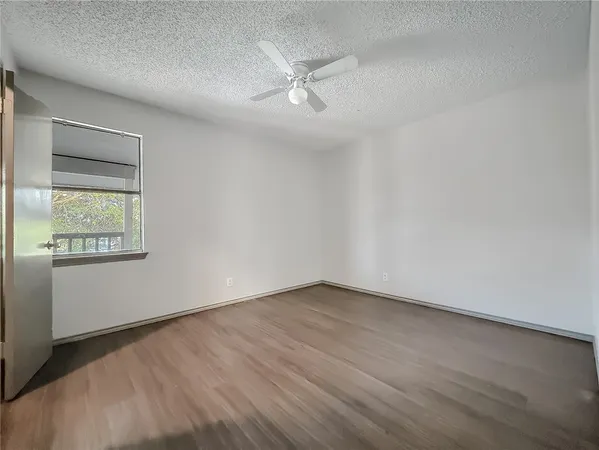 an empty room with wooden floor fan and windows