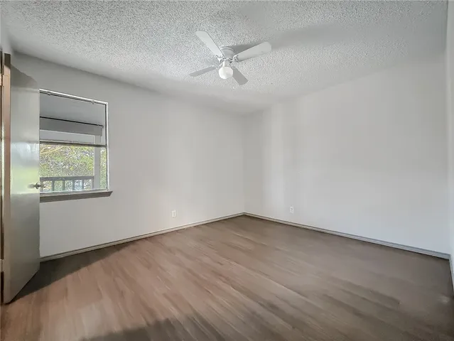 an empty room with wooden floor fan and windows