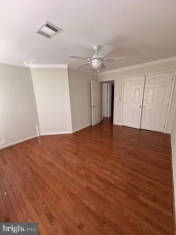 a view of an empty room with wooden floor and a ceiling fan