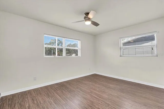 an empty room with wooden floor ceiling fan and windows