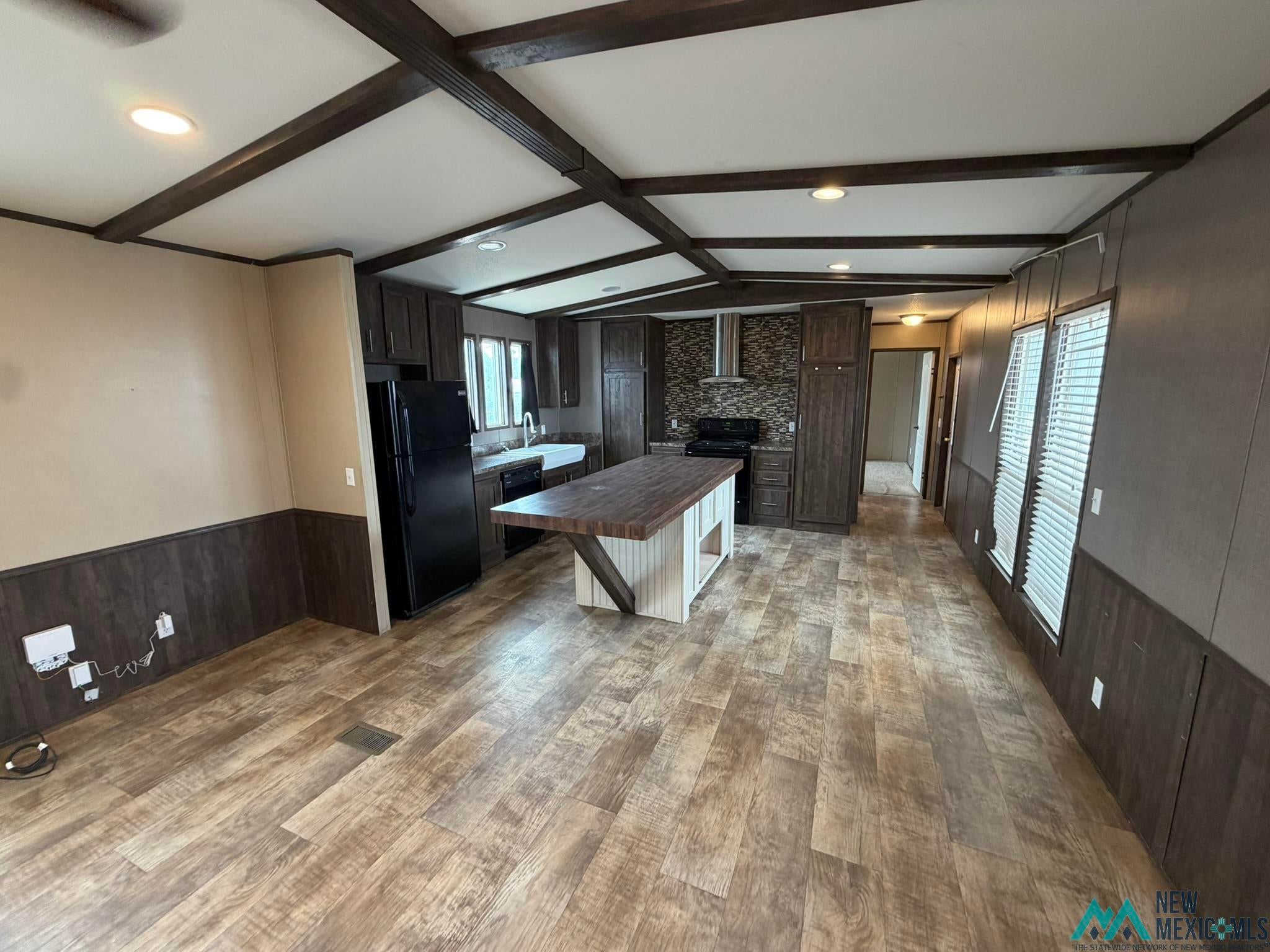 801 Riata Road Carlsbad, NM 88220 - Photo 11 of 39 Open-concept kitchen and living area featuring wood-finish flooring, exposed ceiling beams, a central island with a wood-finish countertop, dark cabinetry, and a subway tile backsplash