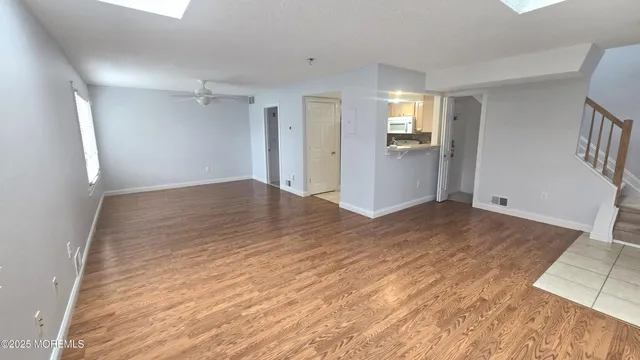 a view of an empty room with wooden floor and a kitchen